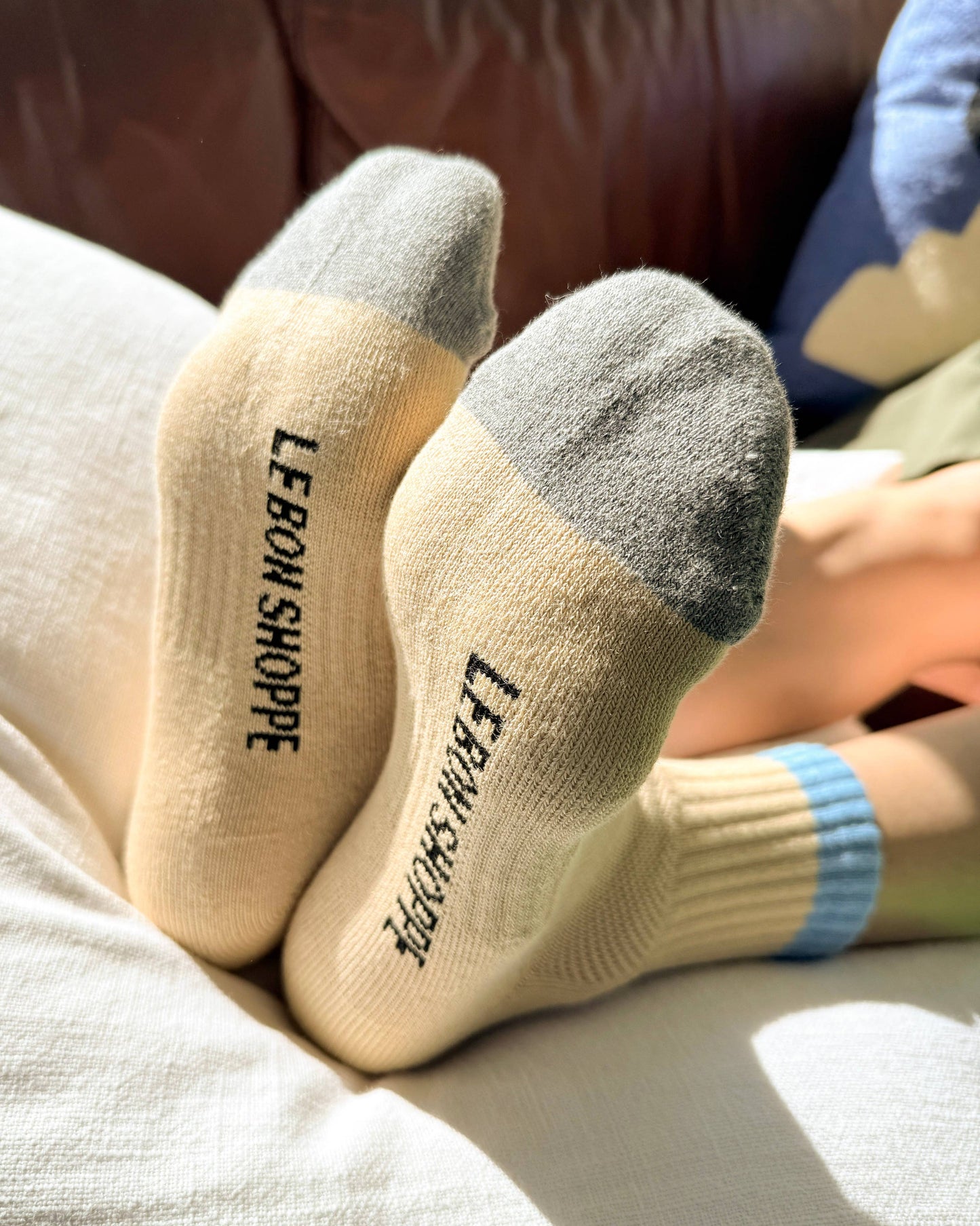 Beige socks with gray toes and 'LEBOW SHOPPE' branding on a couch.