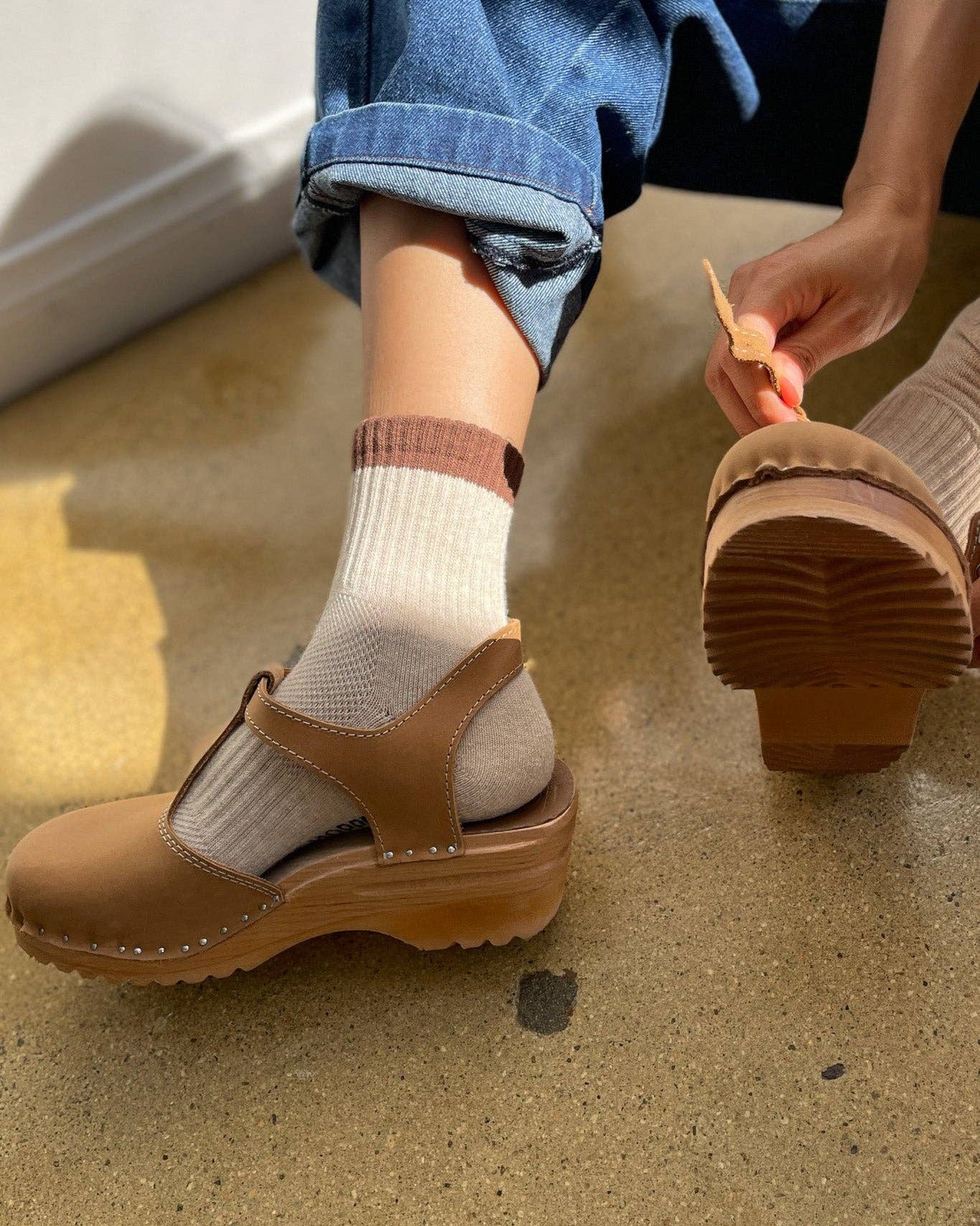 Person wearing brown clogs with white socks on a concrete floor.