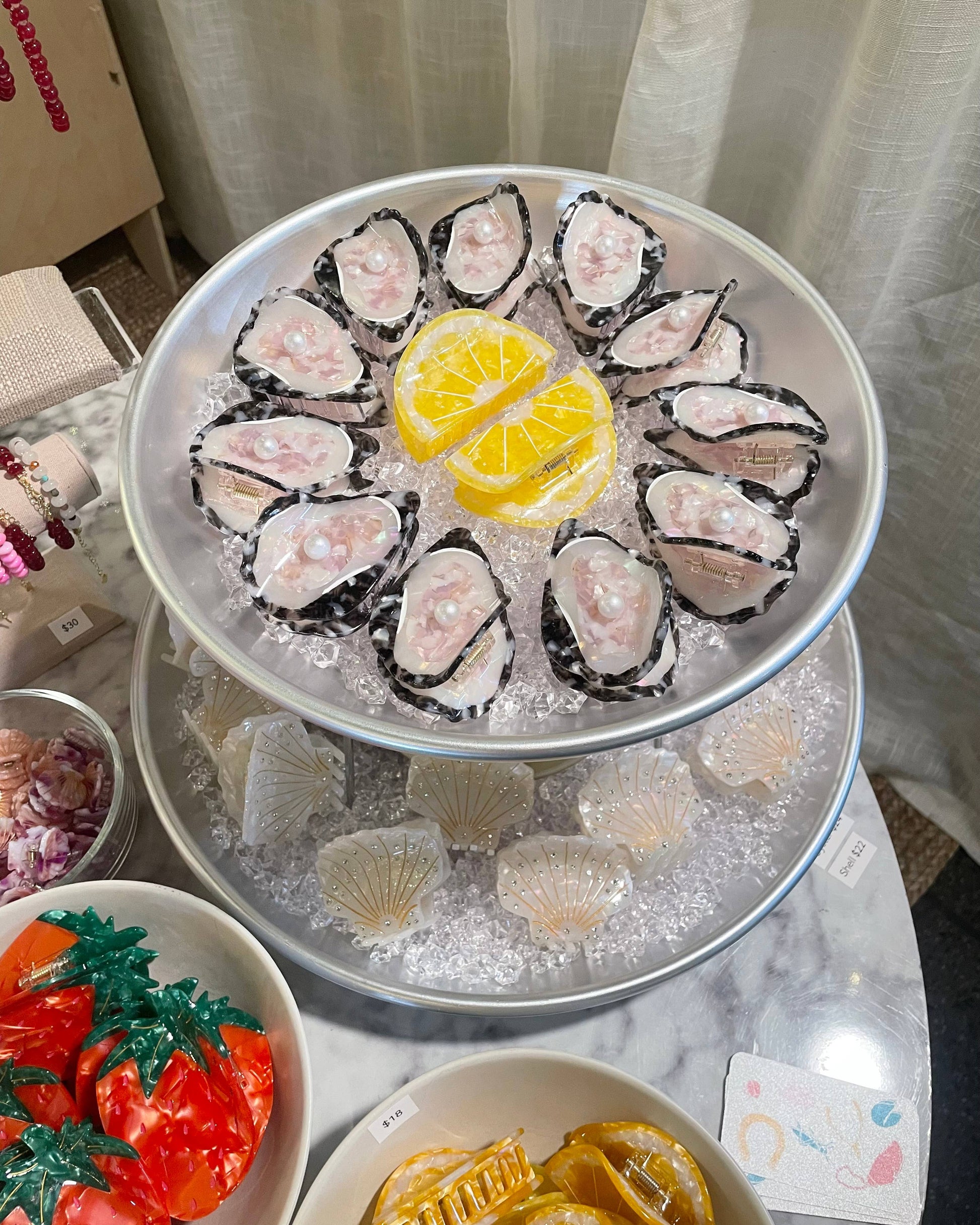 Oyster hair clips on a half shell with lemon hair clip wedges on a bed of ice, laying on a tiered tray 