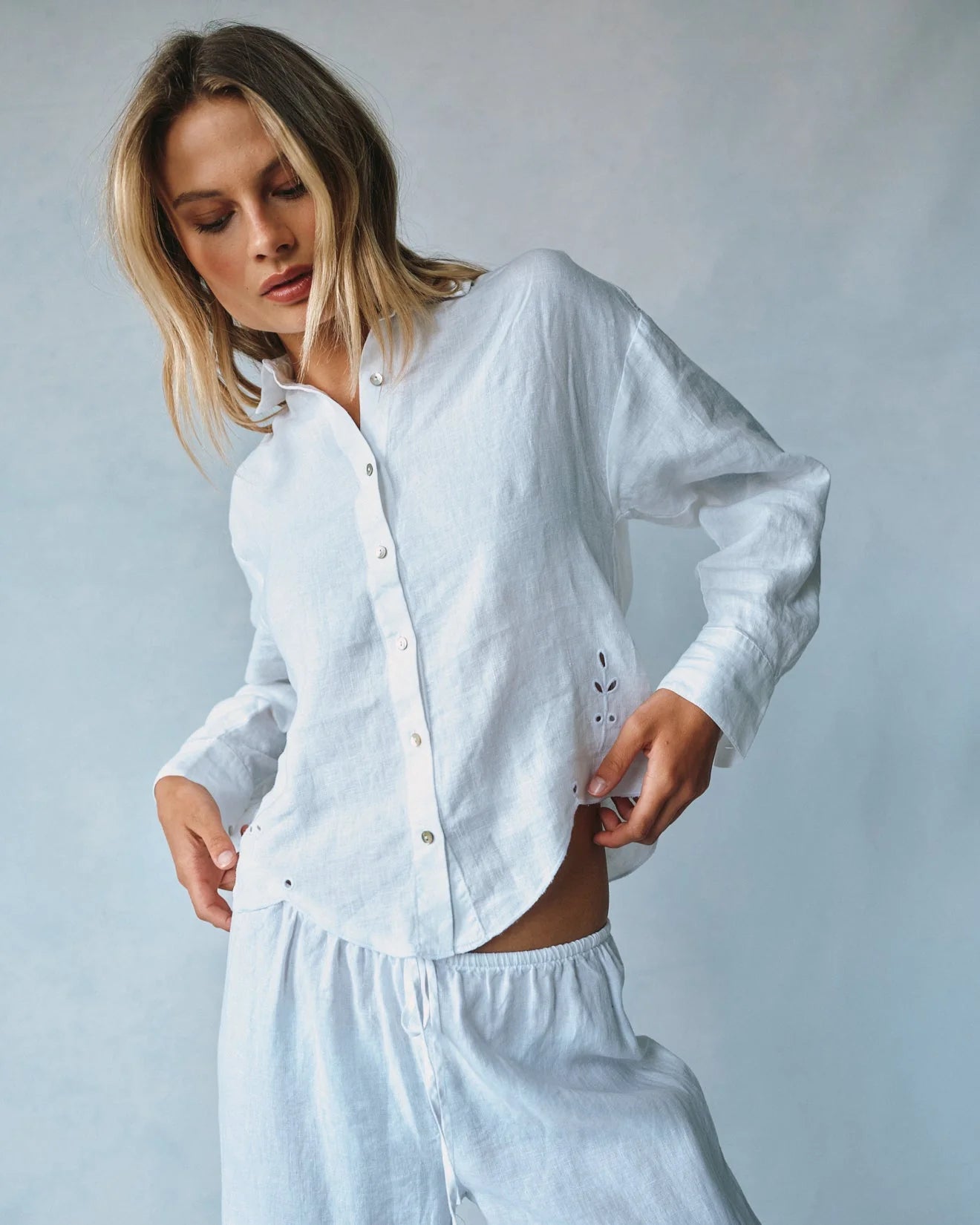 Woman wearing a white linen shirt and pants against a plain background