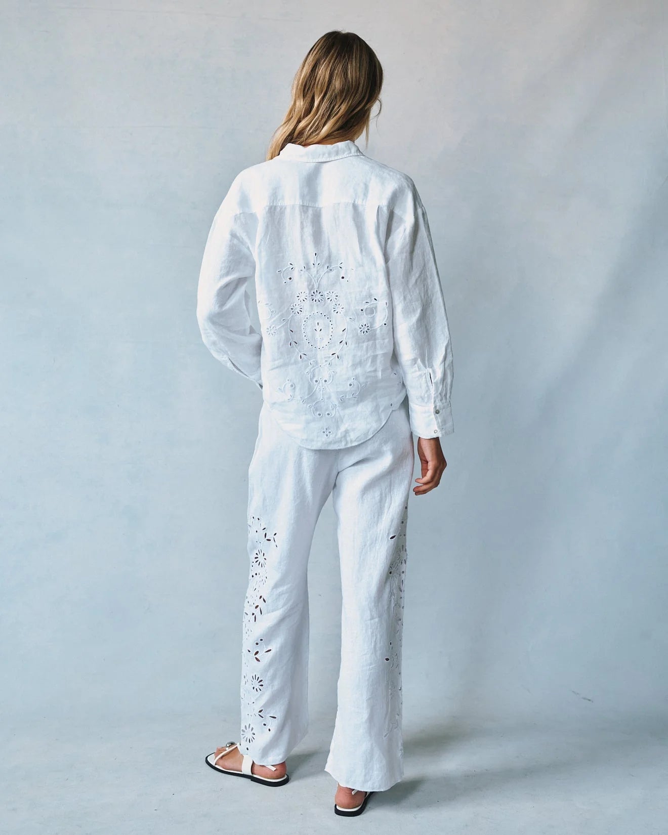 Person wearing a white embroidered outfit against a plain background