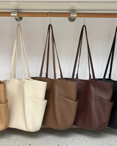 Five leather handbags in different colors hanging on a rack.