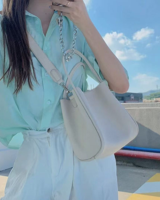 Person holding a beige handbag with a clear sky background