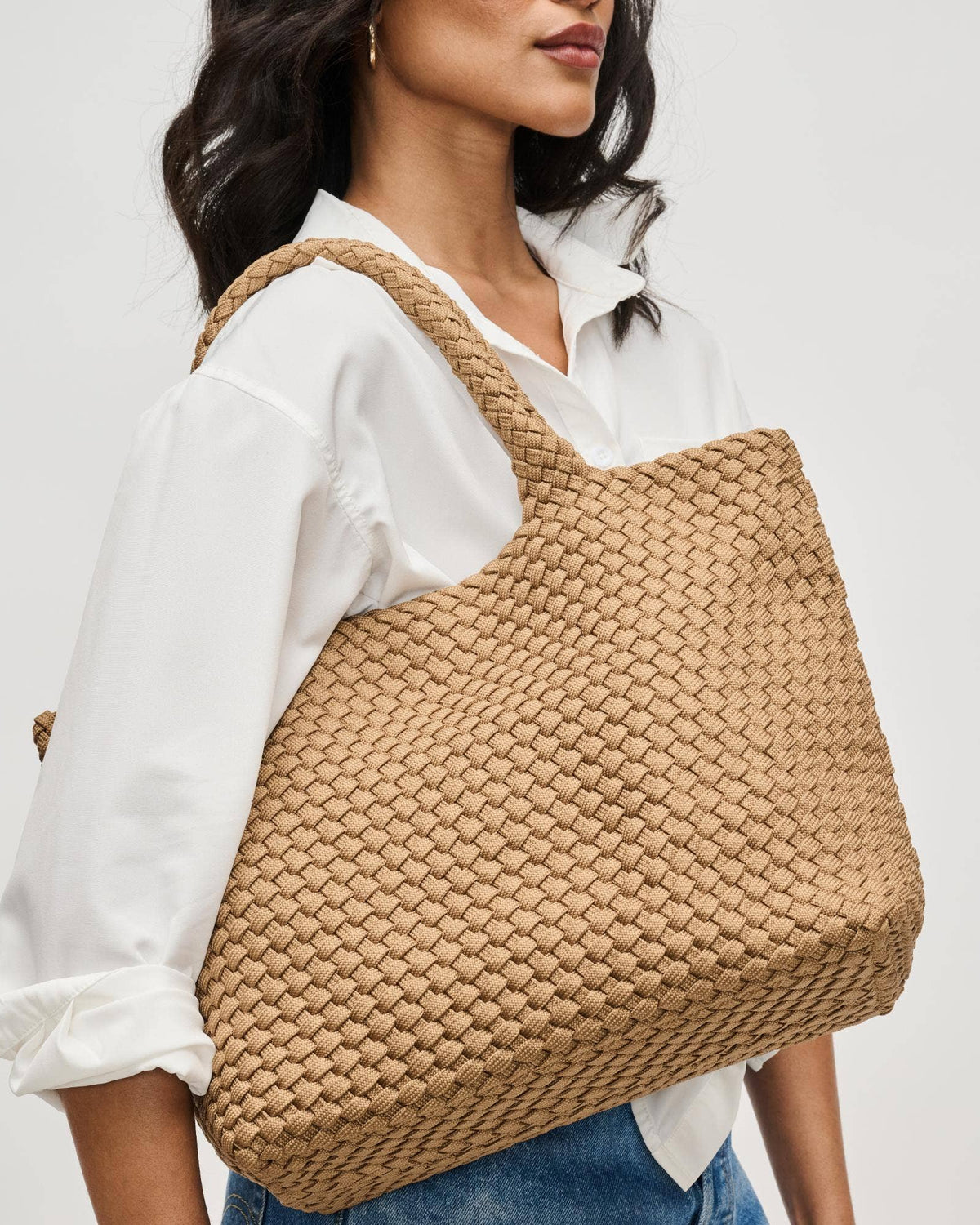 Woman holding a woven beige handbag against a plain background
