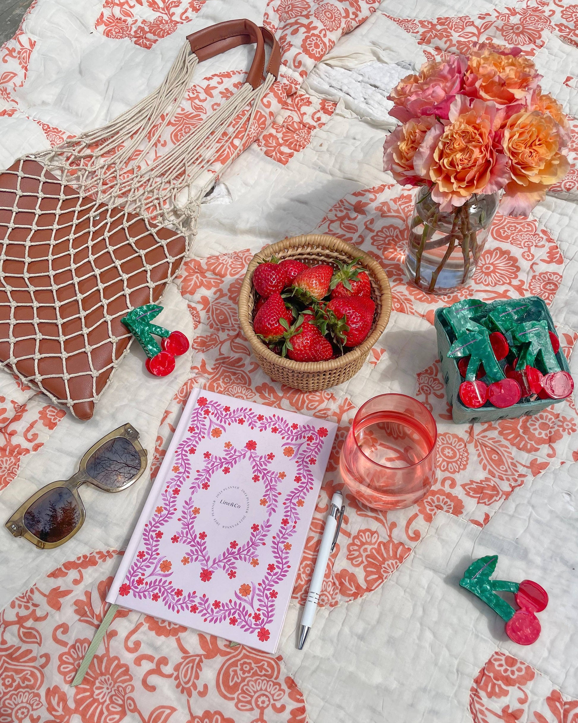 Table setting with strawberries, sunglasses, and cherry shaped hair clips on a patterned tablecloth.