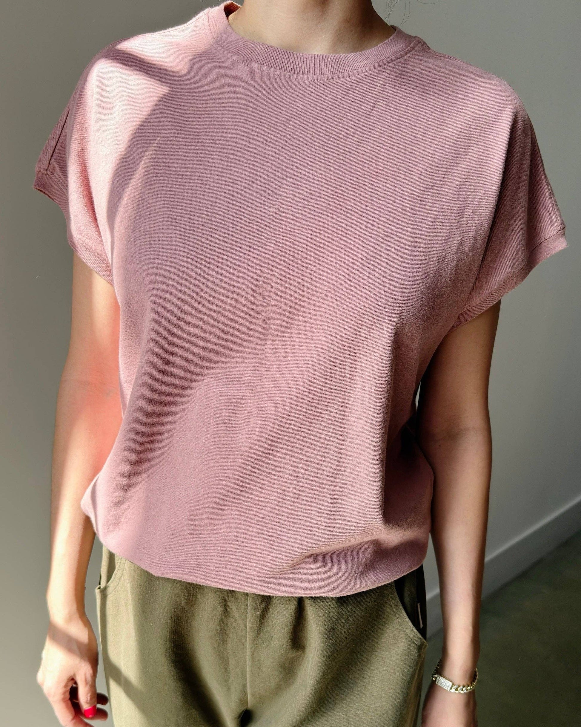 Person wearing a pink t-shirt and green pants against a neutral background
