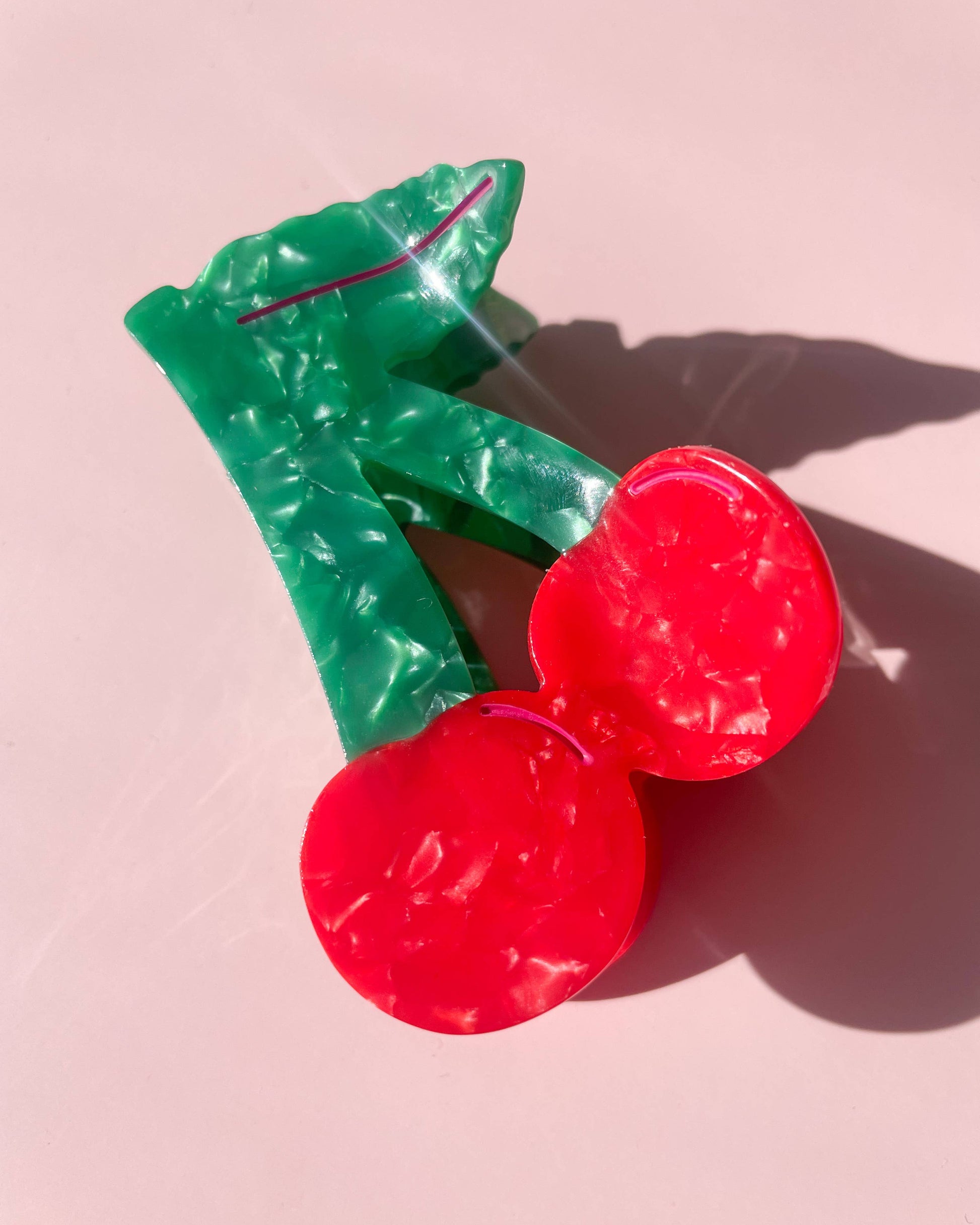 Red cherry-shaped hair clip on a pink background
