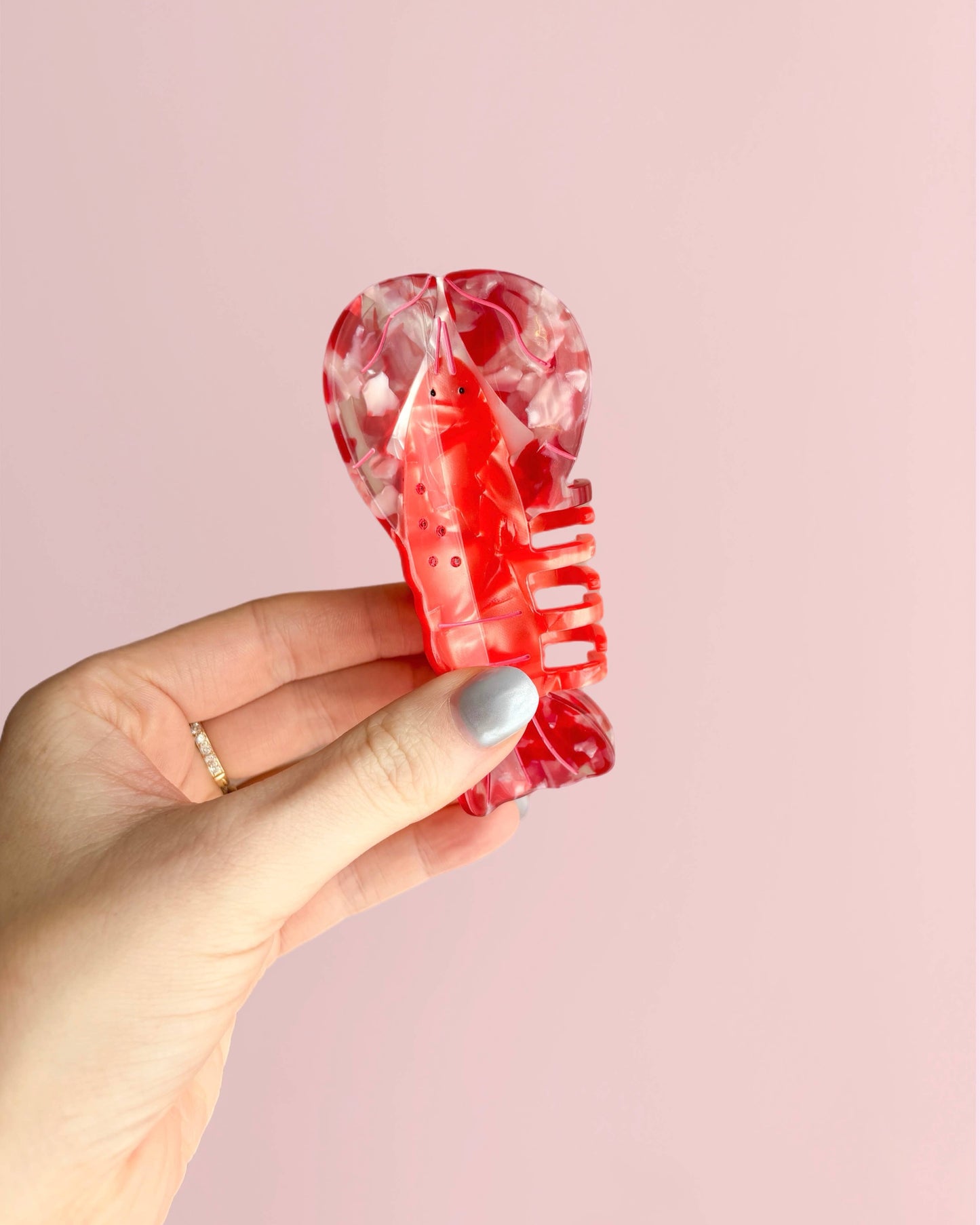 Hand holding a red lobster-shaped hair clip against a pink background