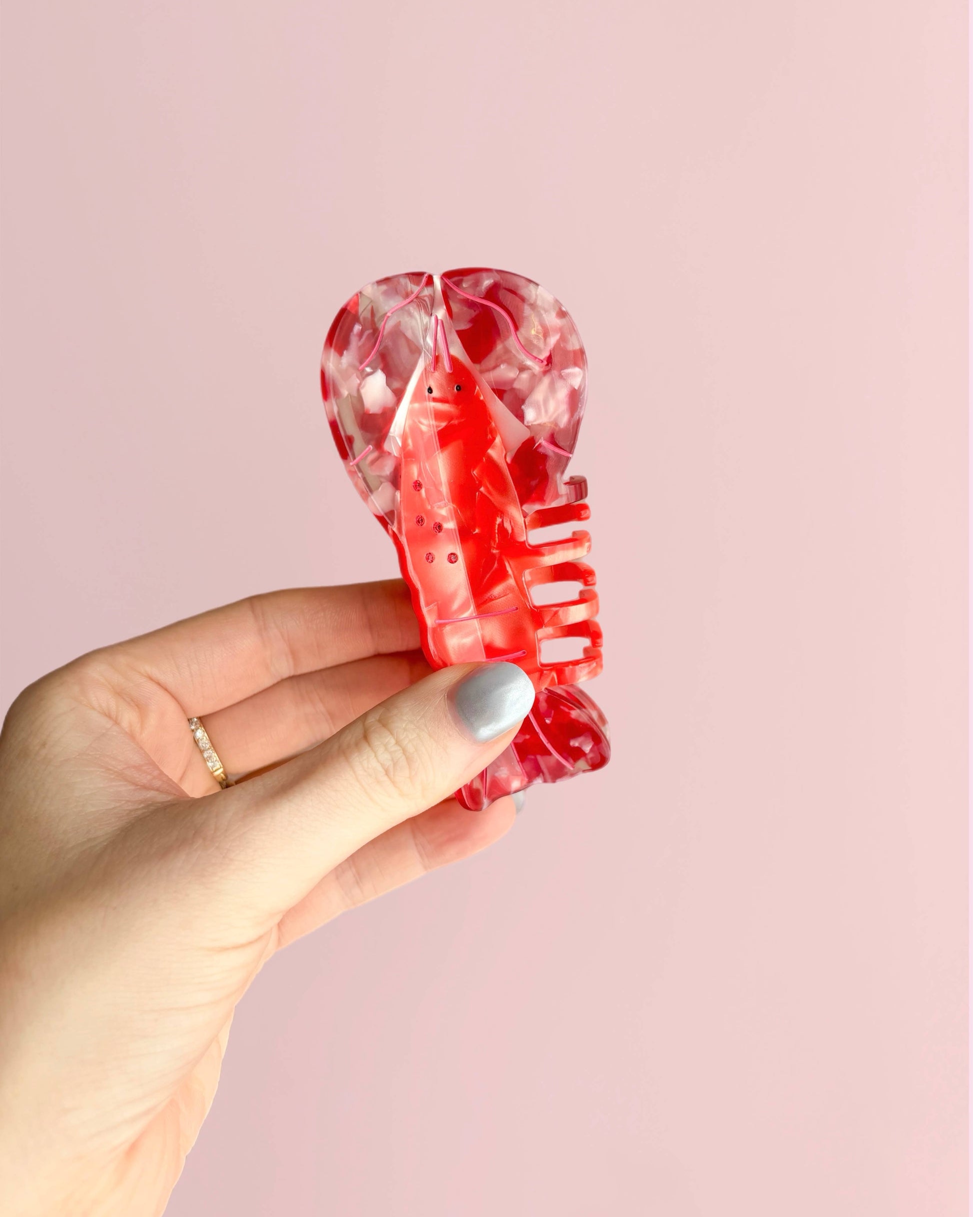 Hand holding a red lobster-shaped hair clip against a pink background