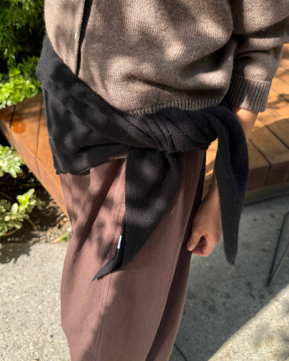 A person outdoors wearing a taupe knit zip-up sweater, dusty mauve wide-leg pants, and a black knit wrap tied around the waist.