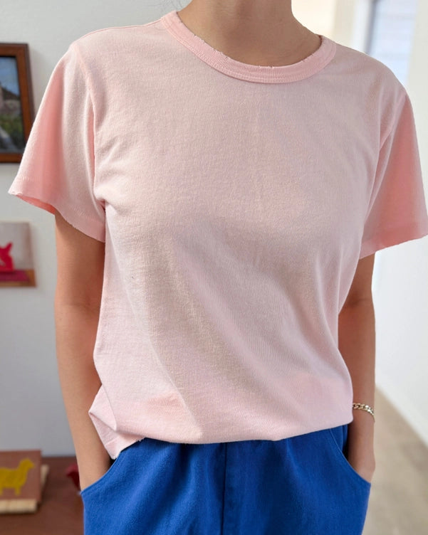 Person wearing a pink t-shirt and blue pants in a room with a wooden desk and framed picture.