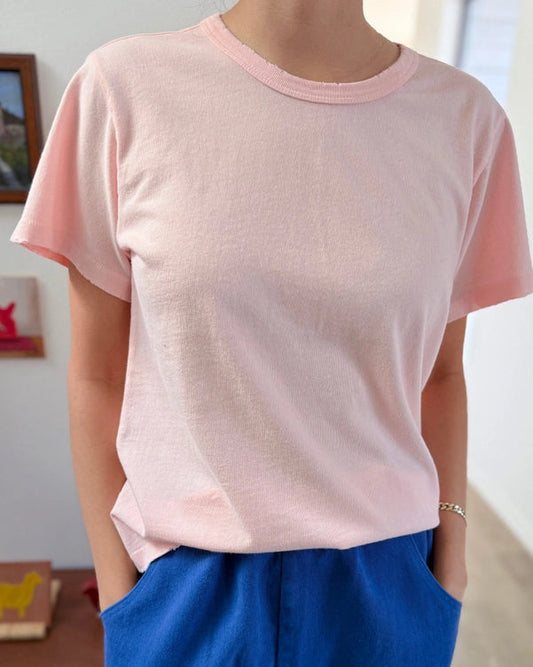 Person wearing a pink t-shirt and blue pants in a room with a wooden desk and framed picture.