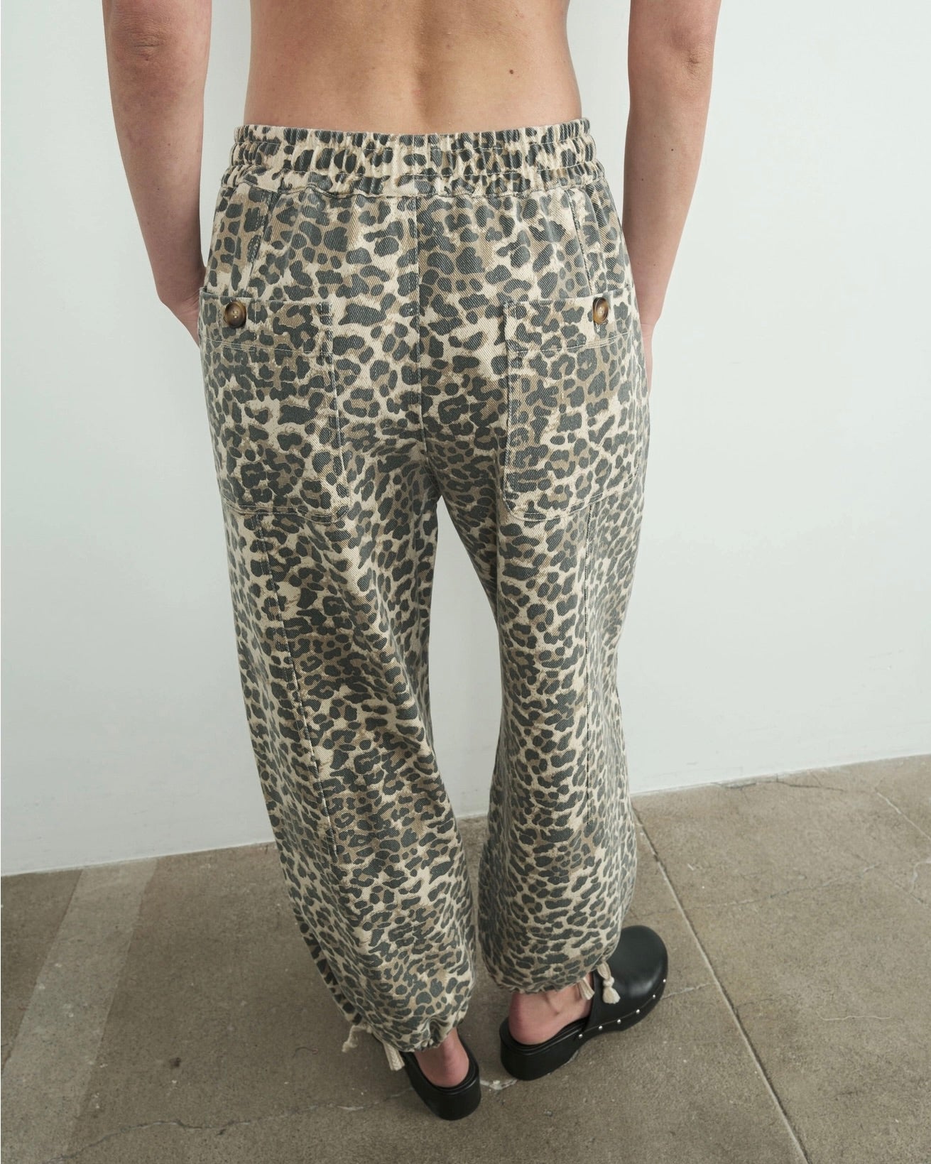 Back view of the Aaron & Amber relaxed fit leopard pull on pant, showing back pocket detail standing in front of a white wall.