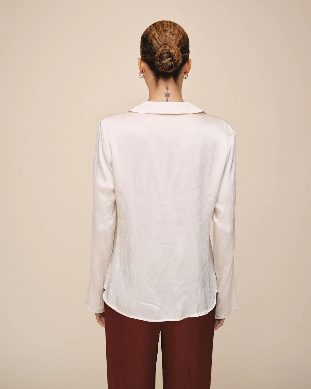 Person wearing a white blouse and maroon pants against a beige background