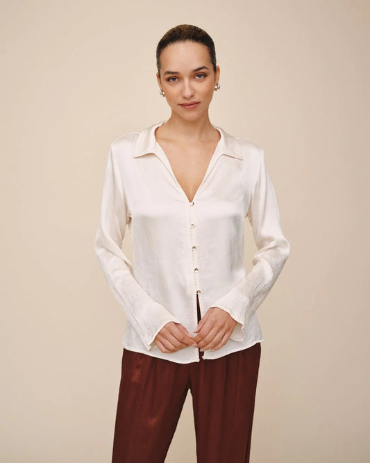 Woman wearing a white blouse and maroon pants against a beige background
