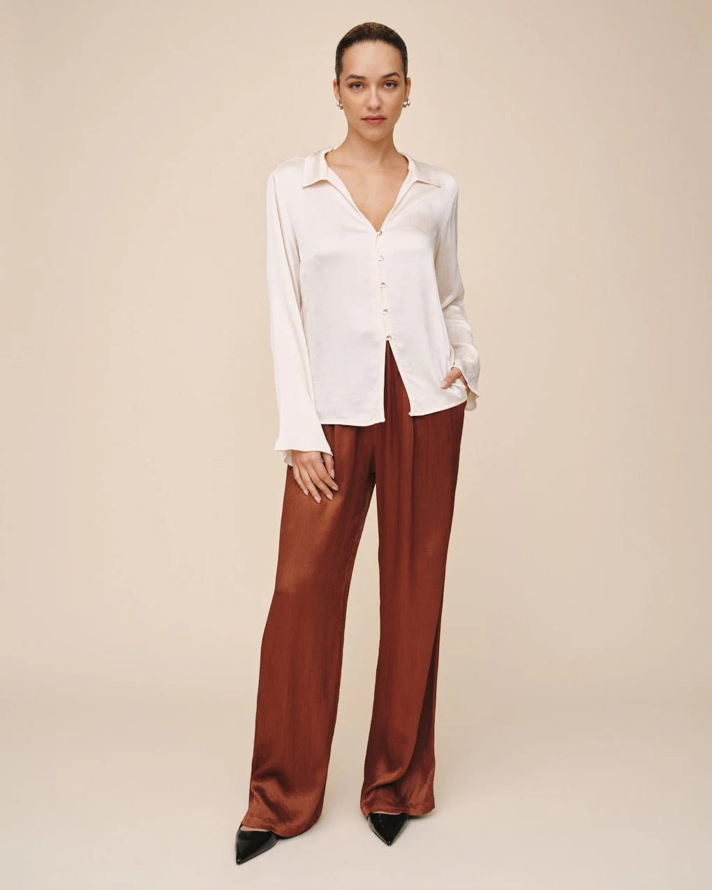 Woman wearing a white blouse and brown pants on a beige background