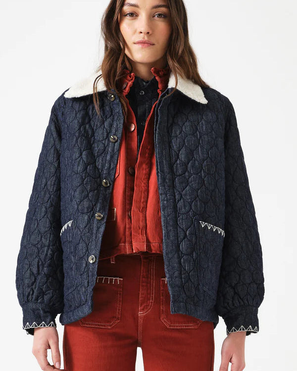 Woman wearing a navy quilted jacket with white collar and red pants on a white background