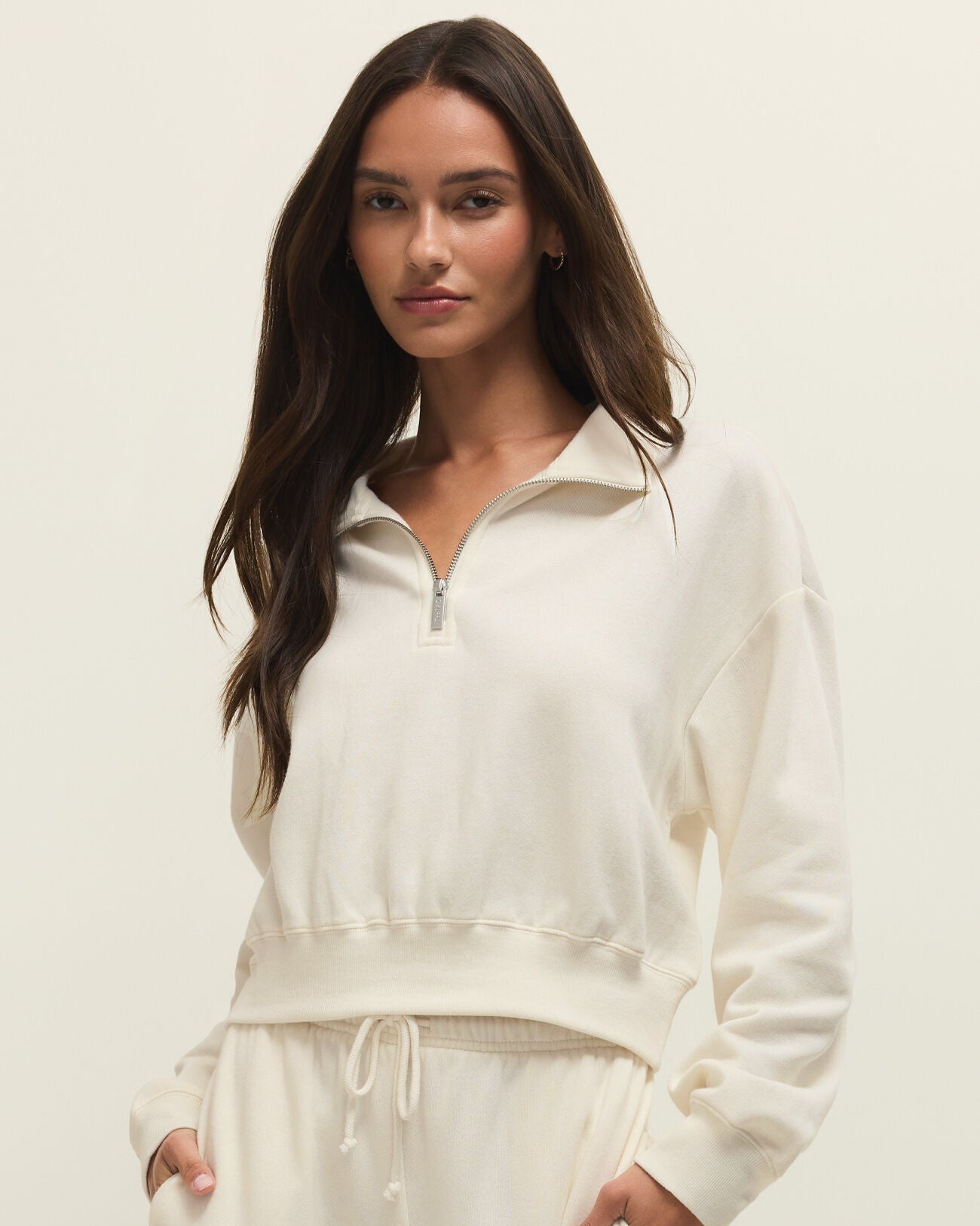 Woman wearing a white zip-up sweatshirt and pants on a plain background