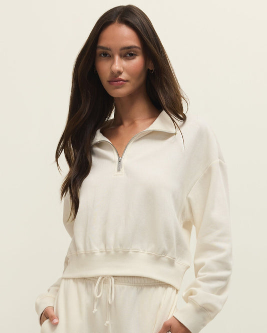 Woman wearing a white zip-up sweatshirt and pants on a plain background