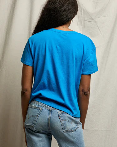 Person wearing a blue t-shirt and jeans standing against a plain background