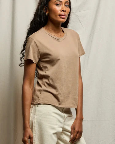 Woman wearing a beige t-shirt and light-colored pants against a neutral background