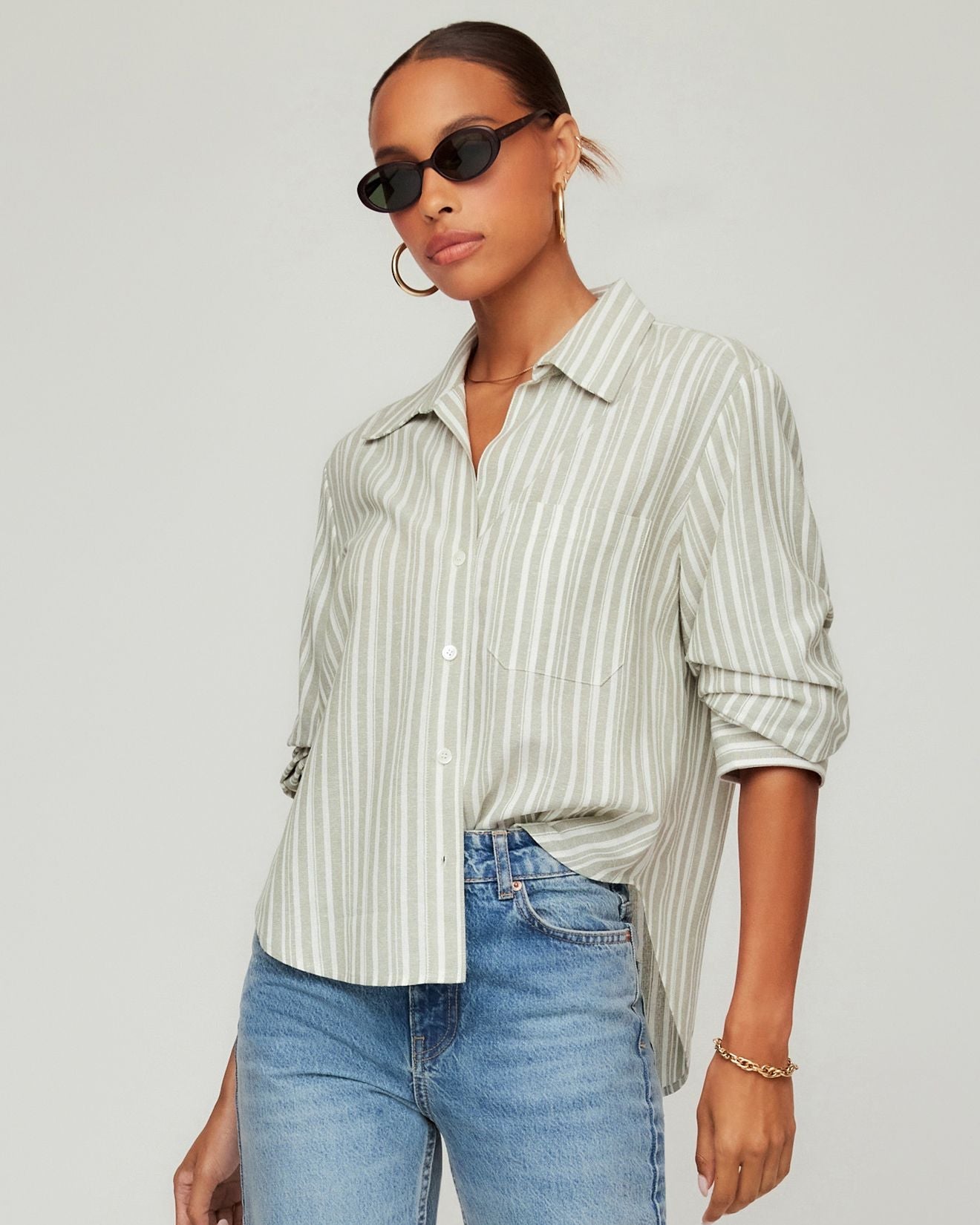 Woman wearing a striped shirt and jeans with sunglasses on a plain background