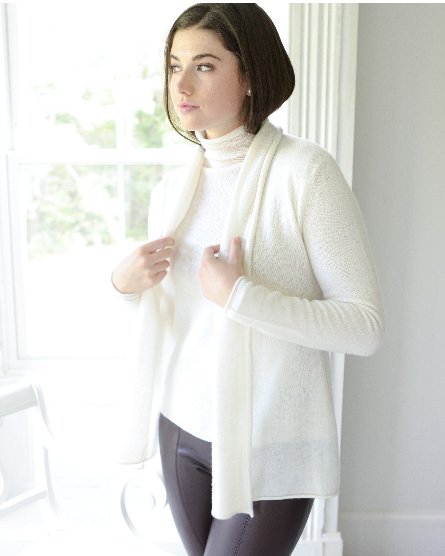 Model wearing Alashan Cashmere mini duster in white wearing white turtle neck and brown paints on a white background