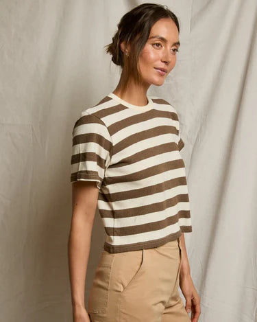 Woman wearing a brown and white striped shirt and beige pants against a neutral background