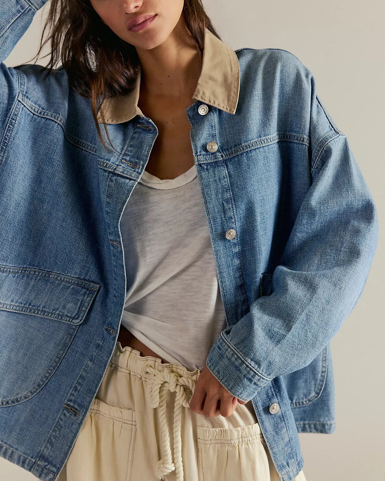Woman wearing a free people lemon denim jacket over a white shirt and beige pants on a neutral background