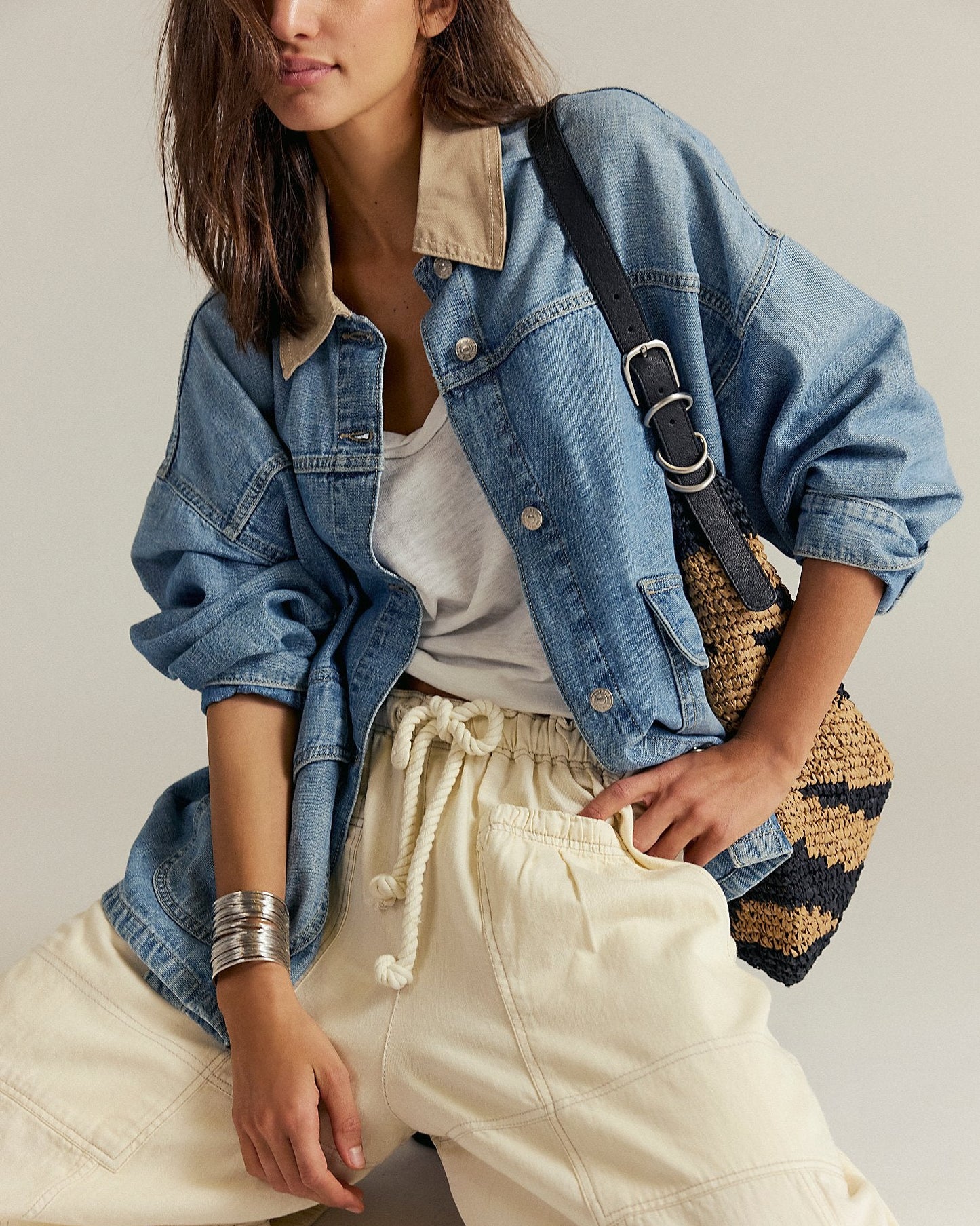 Person wearing a denim jacket, white top, and beige pants with a striped bag.