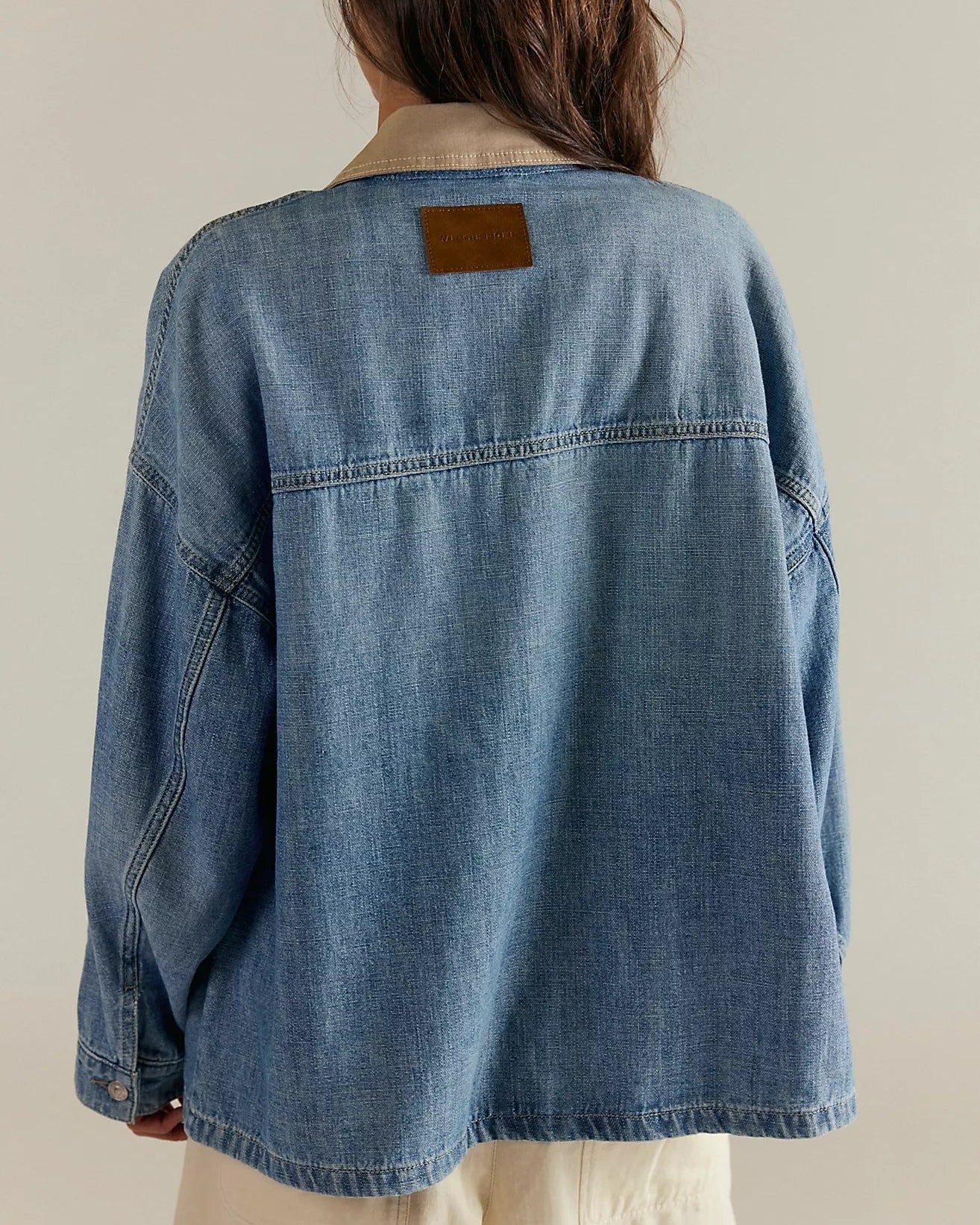 Person wearing a free people denim jacket with a plain background