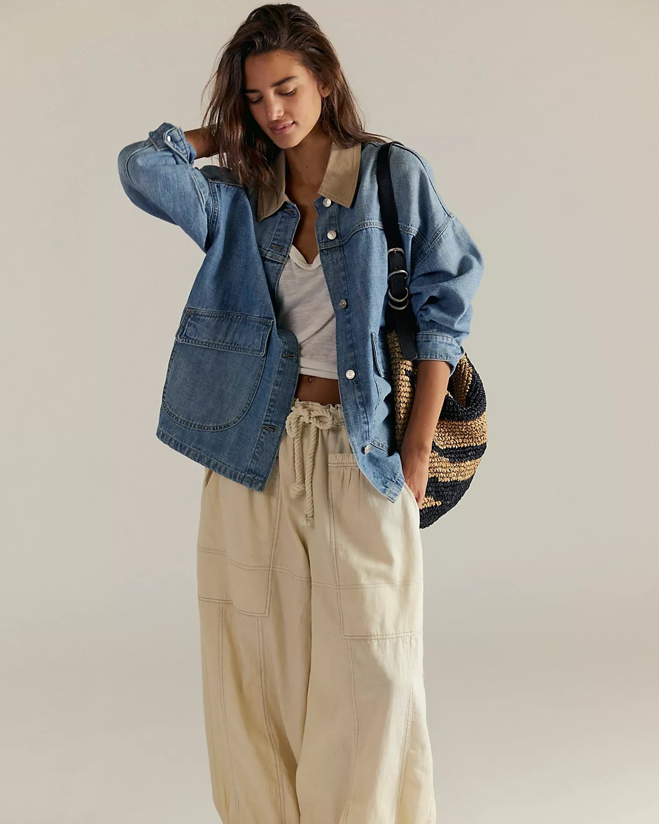 Woman wearing a denim jacket, white top, and beige pants against a plain background