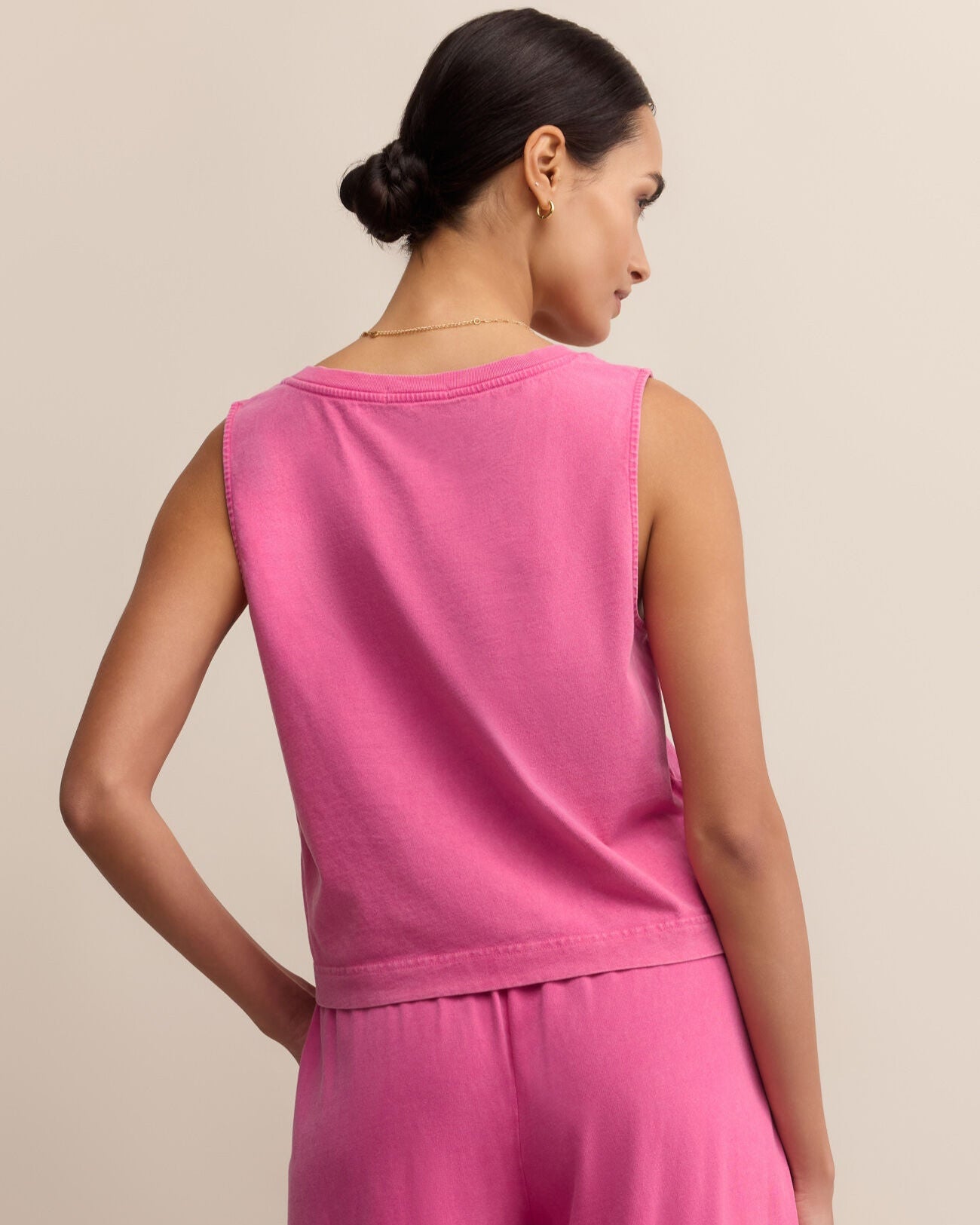 Woman wearing a pink sleeveless top and pants against a beige background