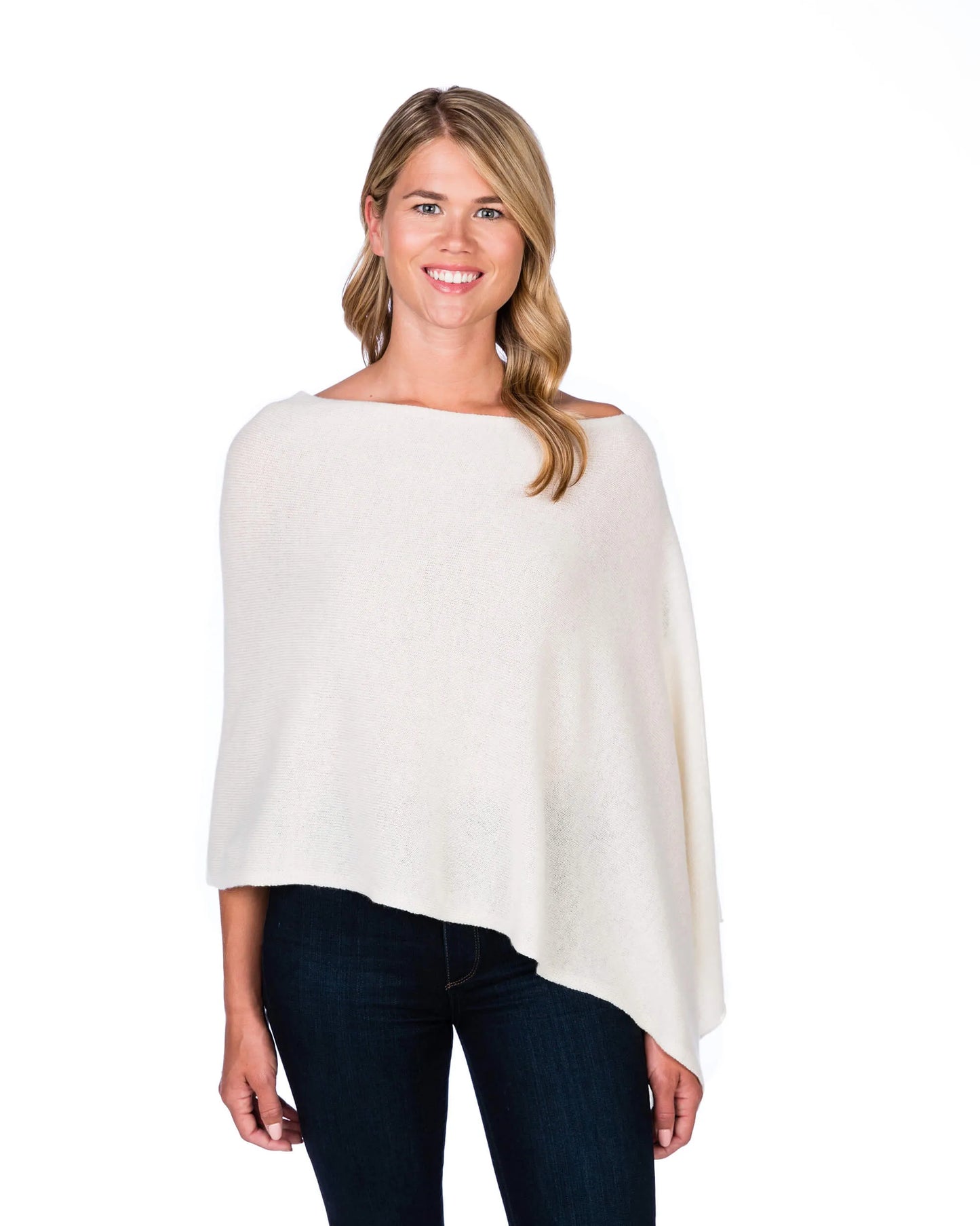 Woman wearing a white poncho over dark jeans on a white background