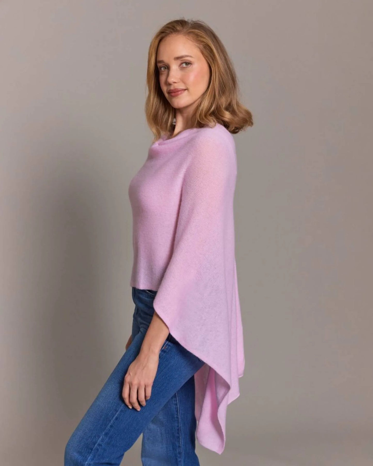 Woman wearing a light pink poncho over a blue outfit against a plain background