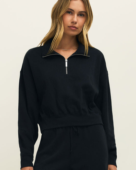 Woman wearing a black zip-up sweatshirt and pants on a beige background