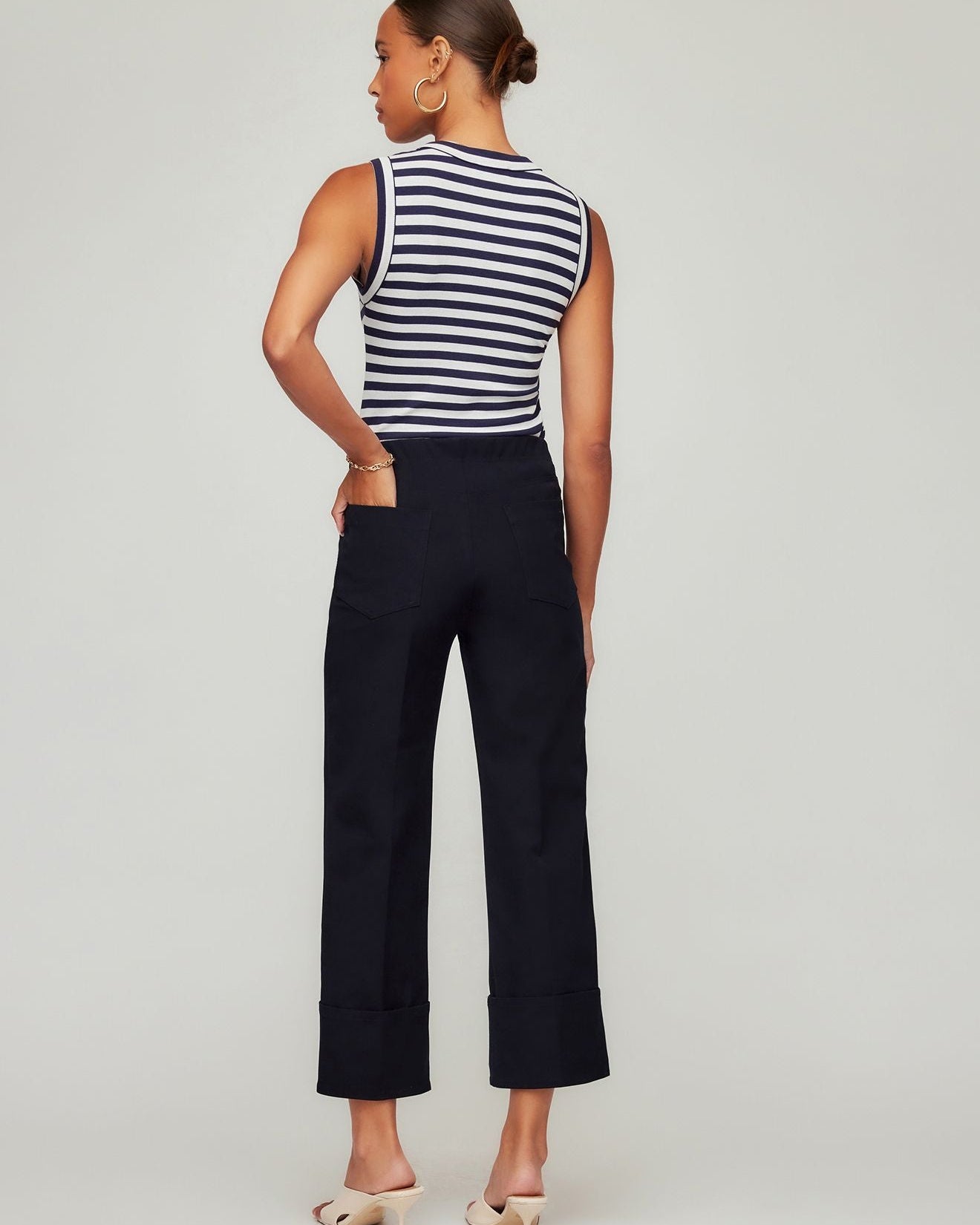 Woman wearing a black and white striped sleeveless top and navy pants on a light gray background