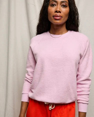 Woman wearing a pink sweater and red pants against a plain background