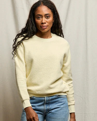 Woman wearing a light yellow sweater and blue jeans against a neutral background
