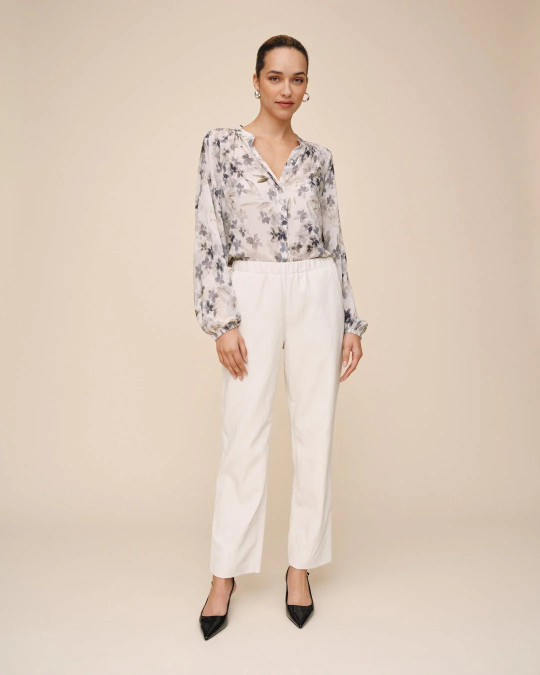 Woman wearing a floral blouse and white pants on a beige background