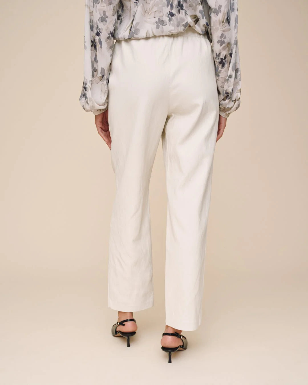 Person wearing a floral blouse and white pants on a beige background