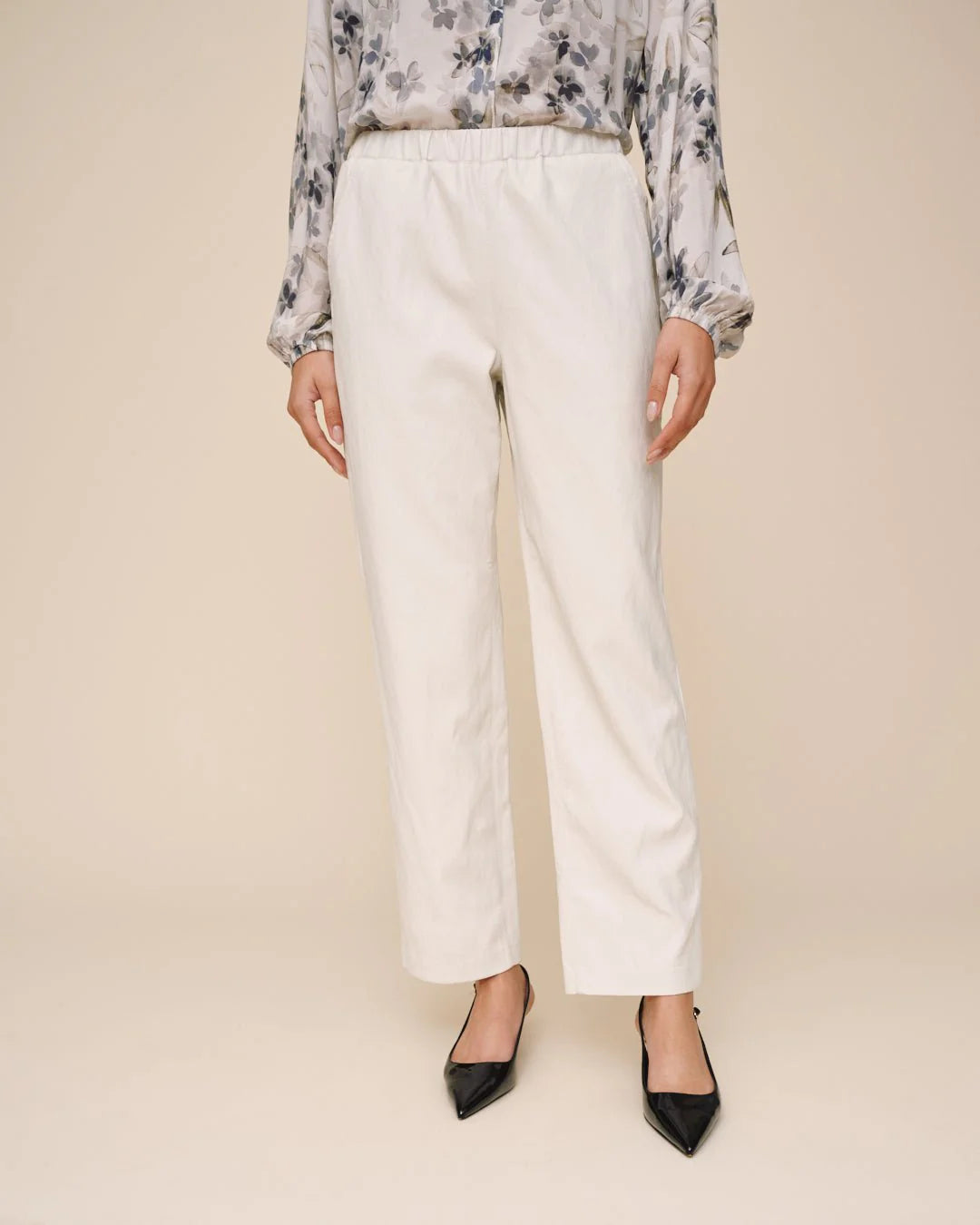 Person wearing a floral blouse and white pants on a beige background