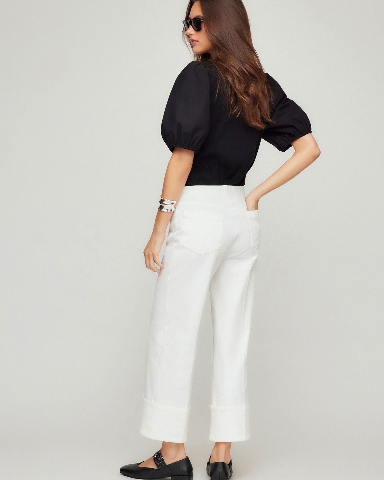 Woman wearing a black top and white pants on a plain background