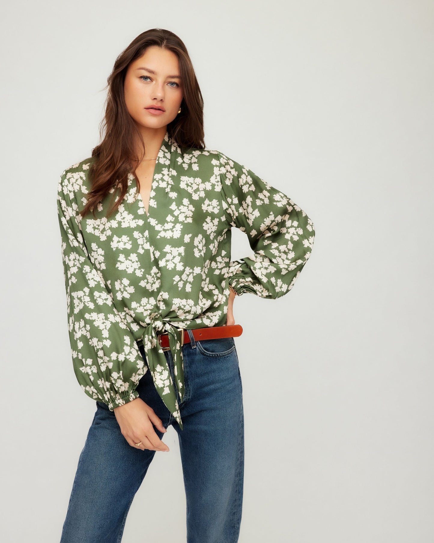 Woman wearing a green floral blouse and blue jeans on a white background