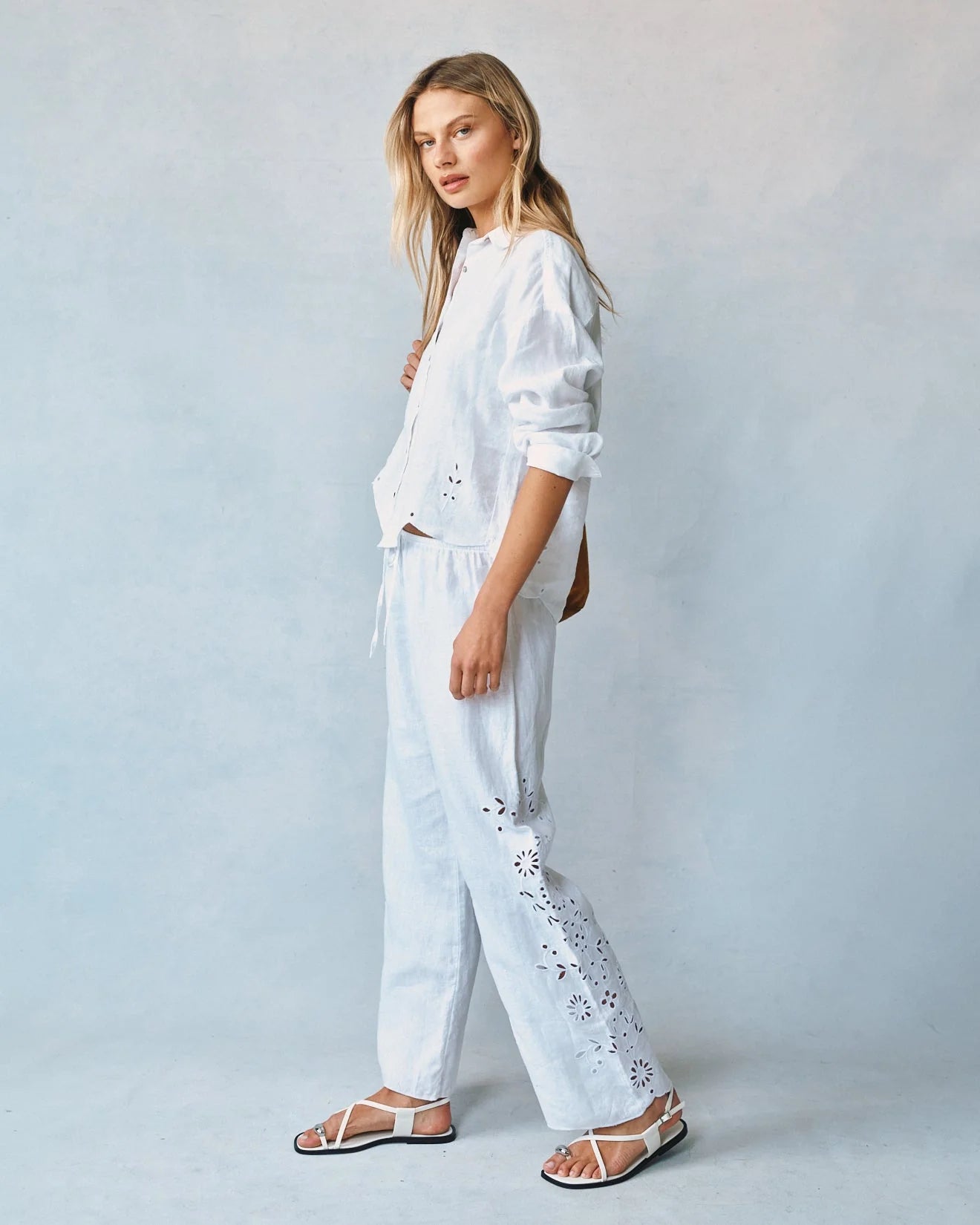 Woman wearing a white outfit with floral embroidery against a light gray background