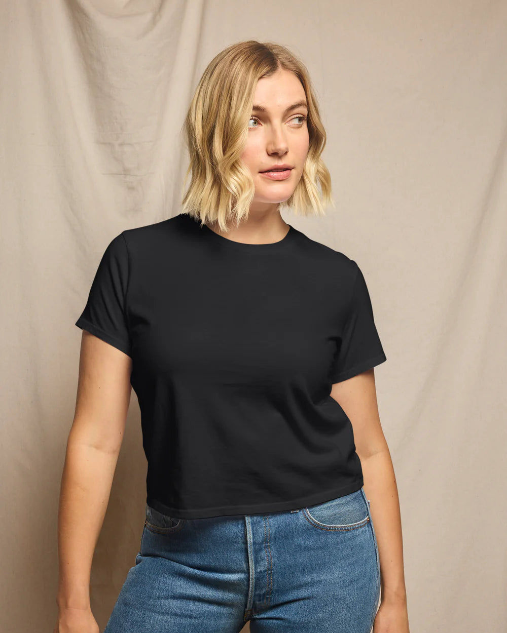 Woman wearing a black t-shirt and blue jeans against a beige background