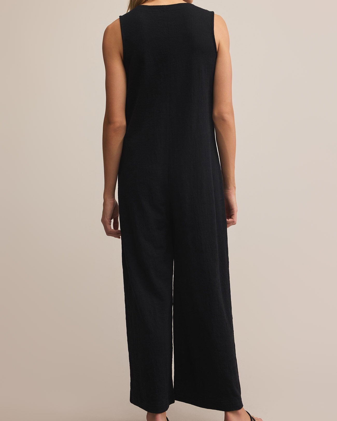 Woman wearing a black sleeveless jumpsuit on a beige background