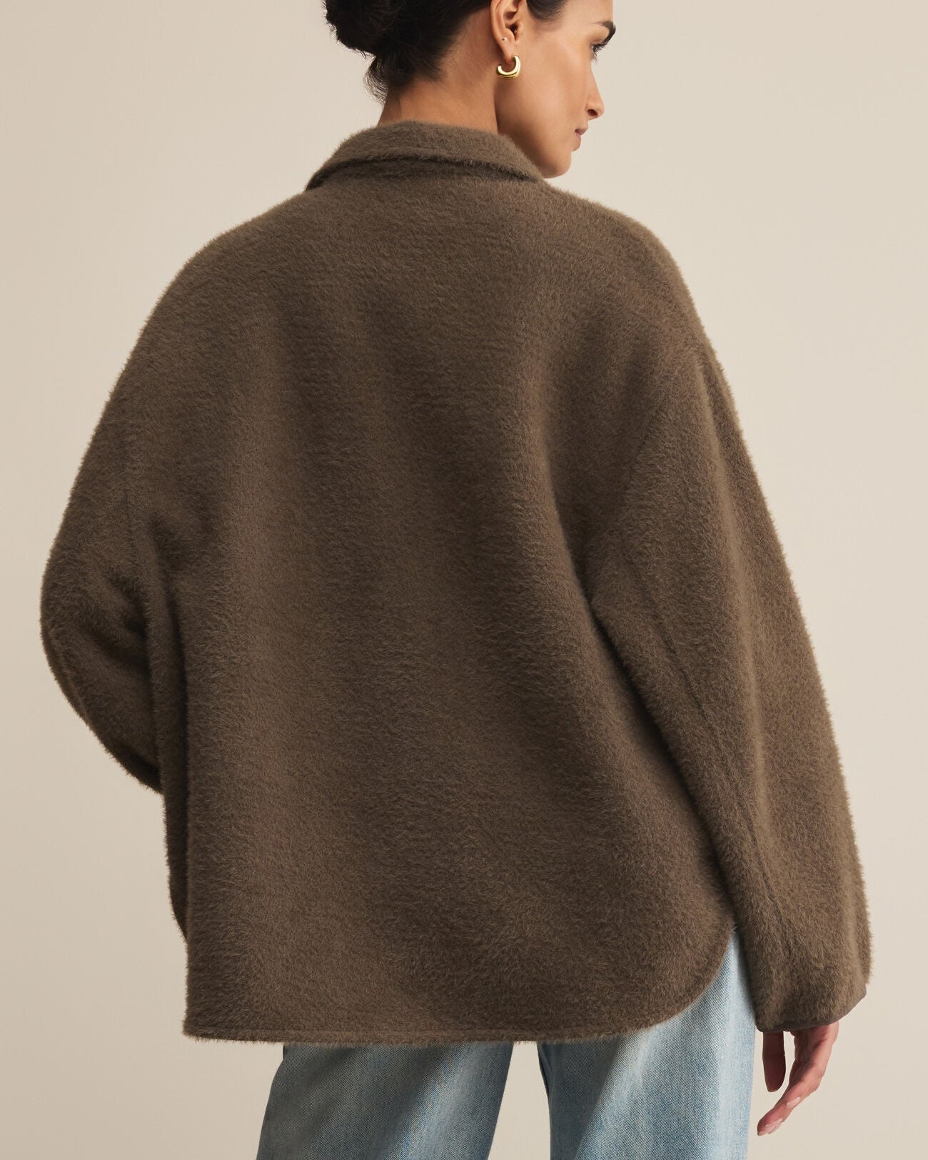 Person wearing a brown coat and light blue jeans against a beige background