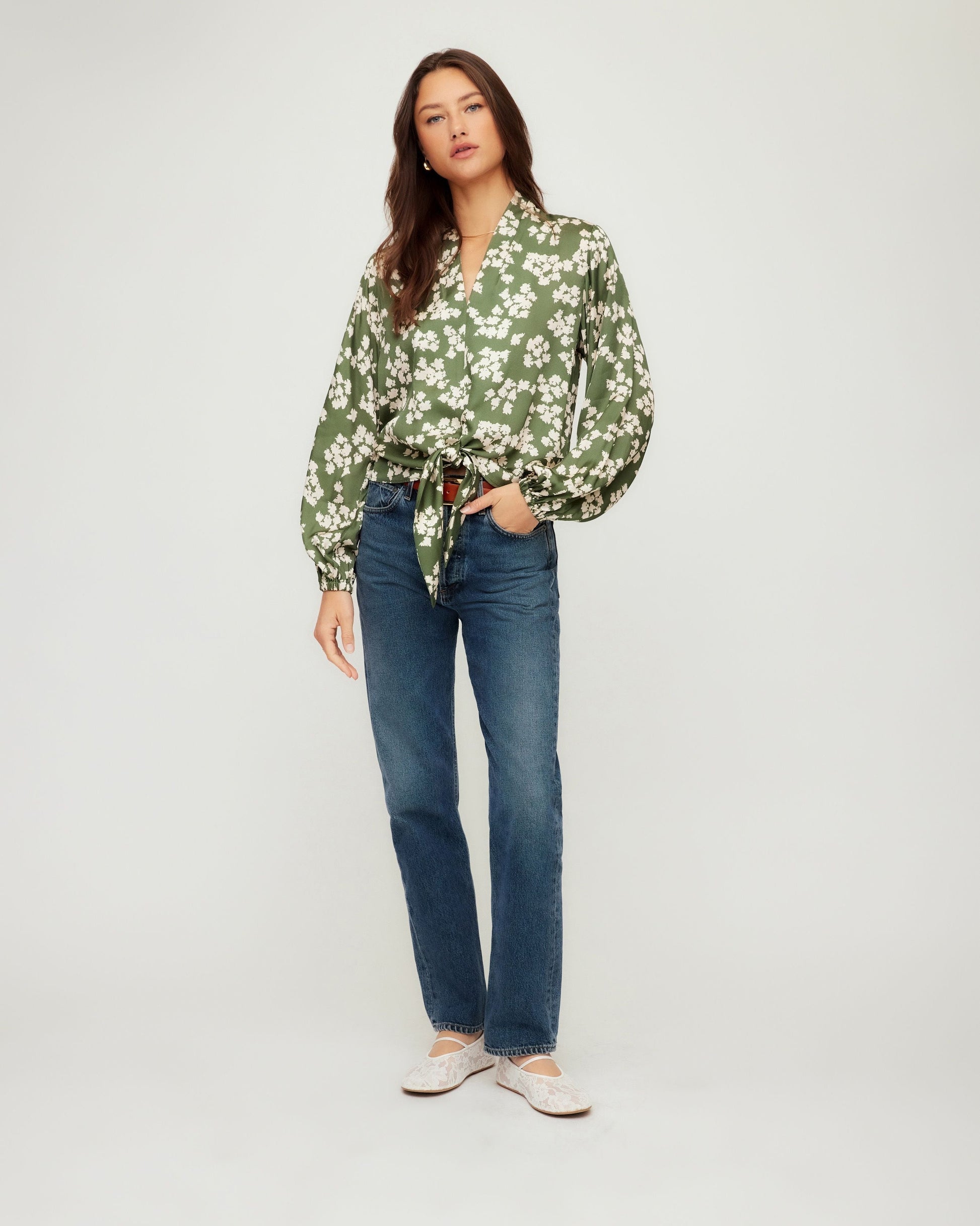 Woman wearing a green floral blouse and blue jeans on a white background