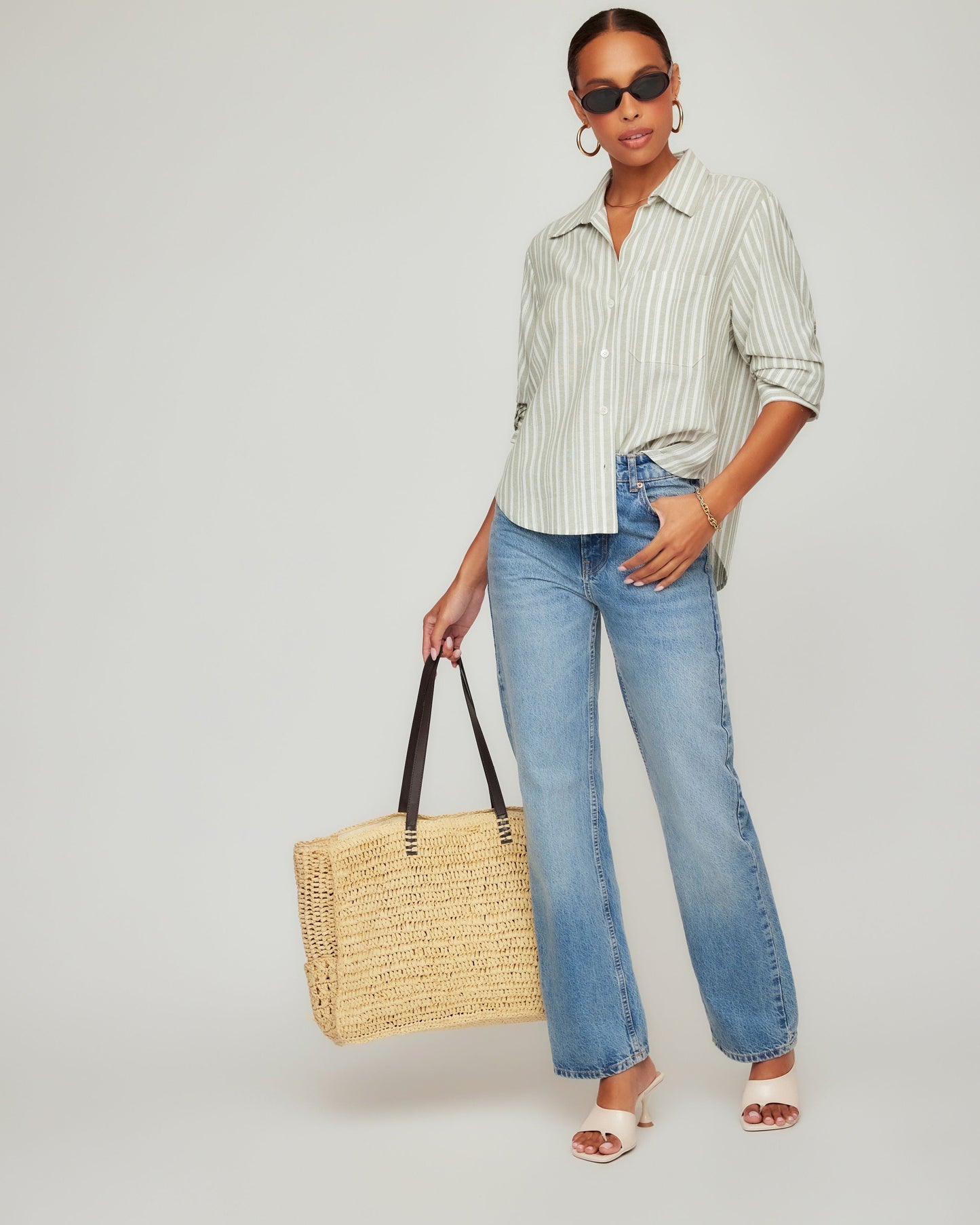 Woman holding a straw bag, wearing a striped shirt and jeans, on a white background